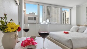 A hotel room with a bed, a vase of flowers, a glass of red wine, and a bowl of chocolate.