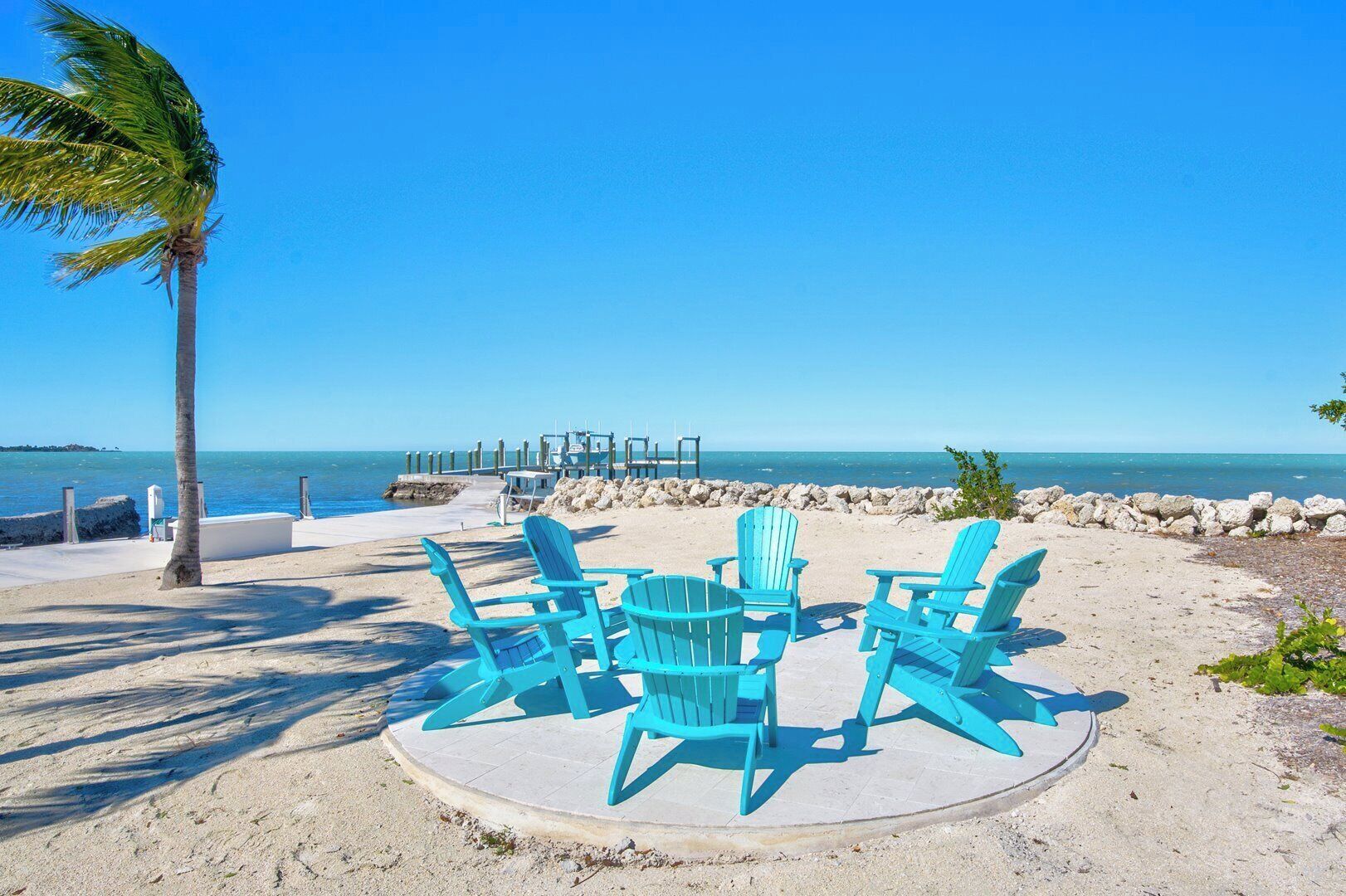 Une plage avec des chaises turquoise, un palmier et une vue dégagée sur l’océan.
