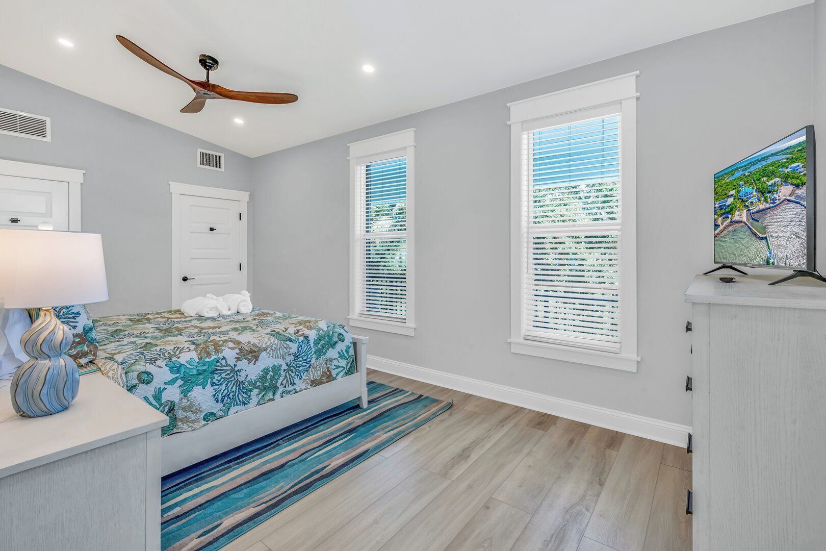 A bedroom with a bed, a ceiling fan, a TV, and a window with blinds.