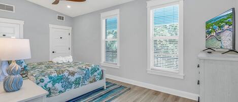 A bedroom with a bed, a ceiling fan, a TV, and a window with blinds.