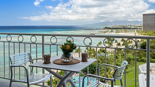 A balcony with a table, chairs, and a view of the ocean and beach. - Ocean View 1-bed/2-bath Penthouse Suite at Waikiki Shore! (Honolulu)