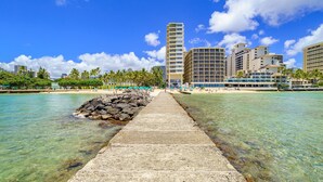 A beachfront hotel with a clear walkway leading to the beach, surrounded by palm trees and clear blue waters. - Ocean View 1-bed/2-bath Penthouse Suite at Waikiki Shore! (Honolulu)