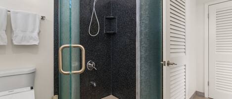Ducha en esquina con mampara de vidrio, inodoro y barra para toallas.