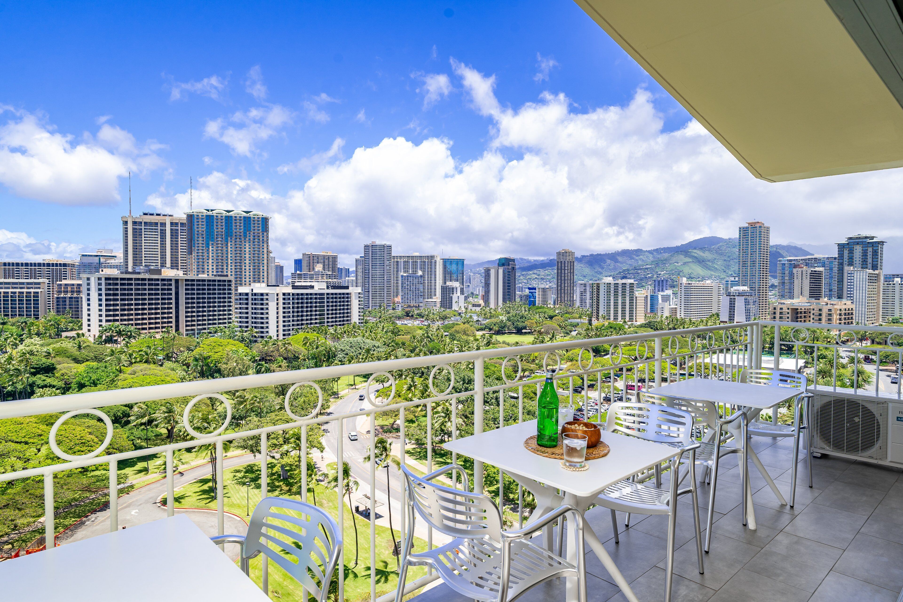A balcony with outdoor seating, a city skyline view, and a green bottle on the table.