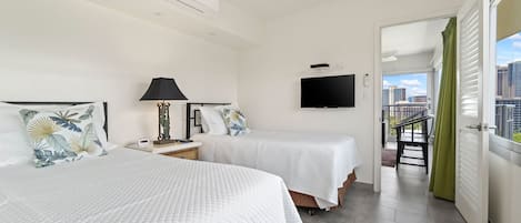 Habitación de hotel con dos camas, televisión y balcón con vista a la ciudad.