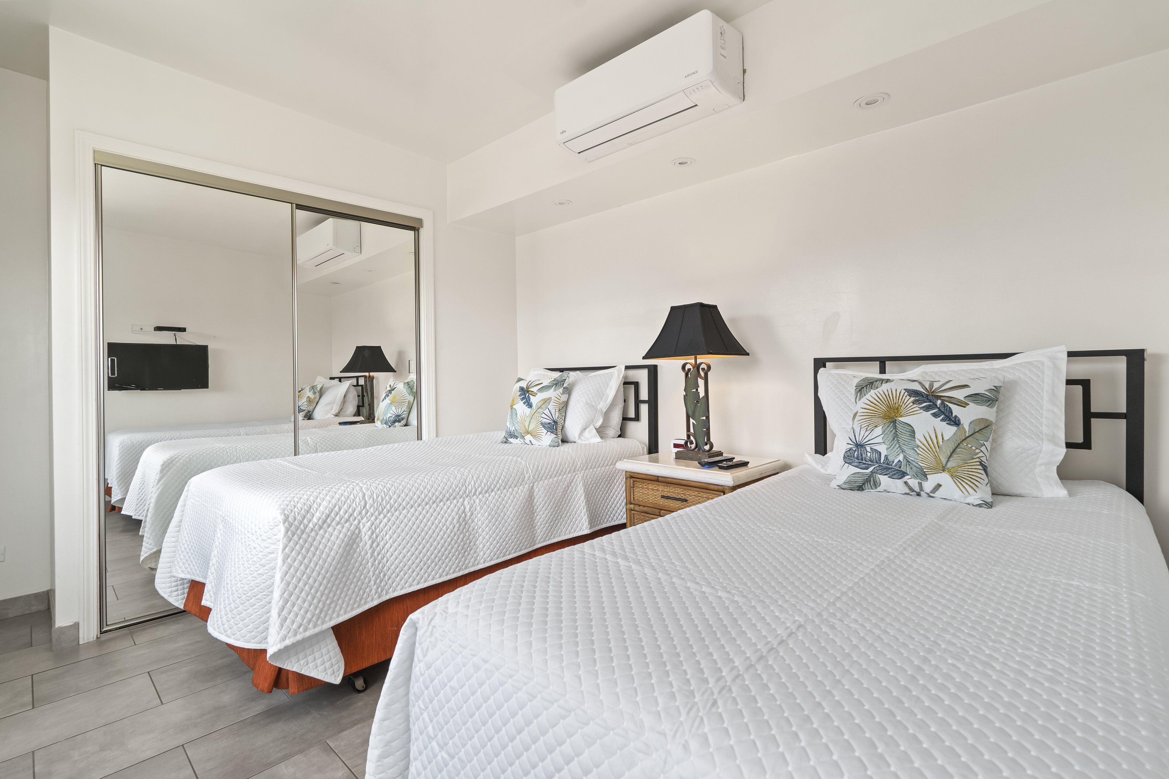 A hotel room with two beds, a mirror, a TV, and a lamp.