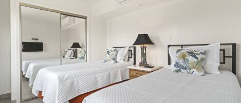 A hotel room with two beds, a mirror, a TV, and a lamp.
