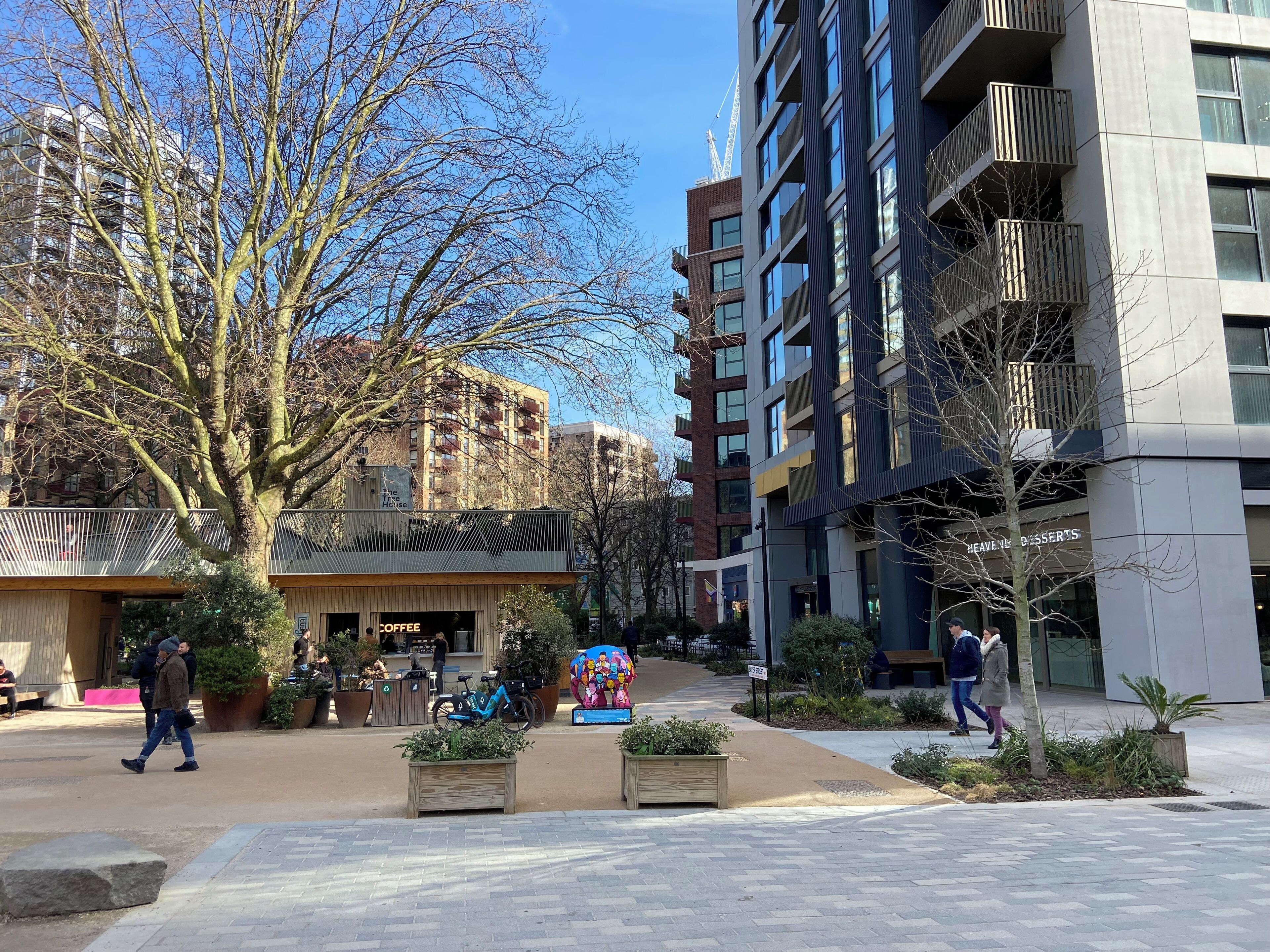 Ein moderner Stadtplatz mit einem Café, einer Konditorei und einem Gebäude mit Balkonen.