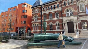 A modern building with a classical facade, a large green sculpture, and a person walking by.