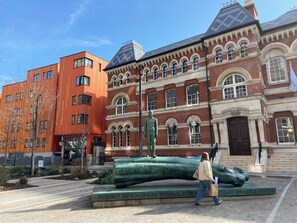 A modern building with a classical facade, a large green sculpture, and a person walking by.