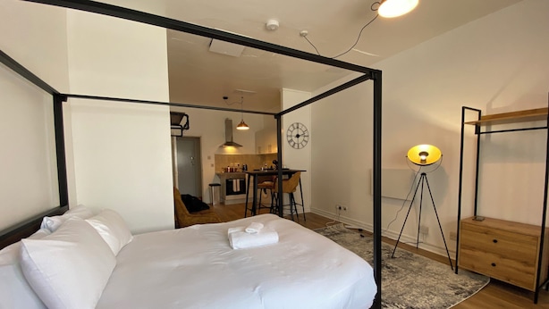 A modern bedroom with a four-poster bed, a small kitchenette, and a dining area. - Premium studio Flat in zone 1 (London)