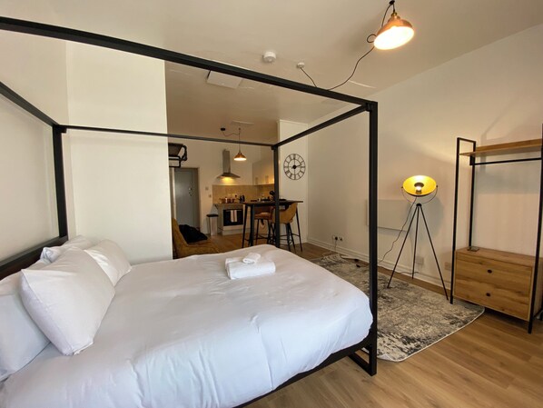 A modern bedroom with a four-poster bed, a small kitchenette, and a dining area.