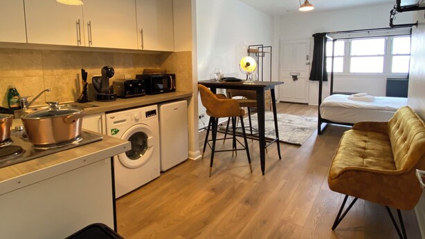 A compact kitchen with a washing machine, a dining area with a table and chairs, and a sofa in a living area.