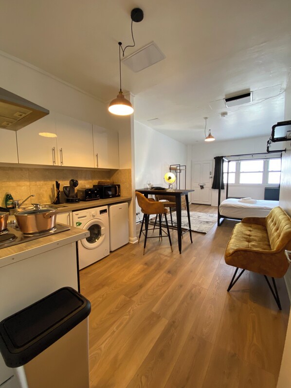 A compact kitchen with a washing machine, a dining area with a table and chairs, and a sofa in a living area.