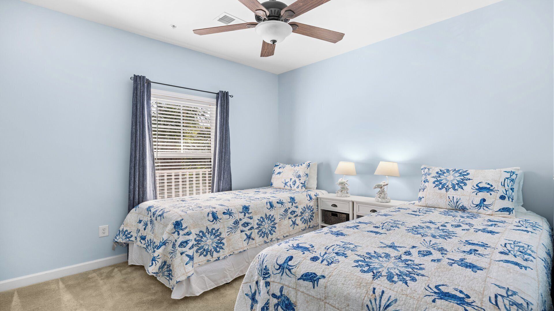 A bedroom with two beds, a ceiling fan, a window with blinds, and bedside lamps.