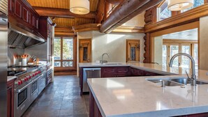 Une cuisine spacieuse dotée d’un grand îlot central, d’appareils électroménagers en acier inoxydable et de poutres en bois au plafond.