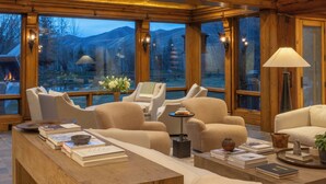 Une pièce spacieuse avec un plafond haut, des poutres en bois, de grandes fenêtres et un coin salon confortable avec des canapés et une table en bois.
