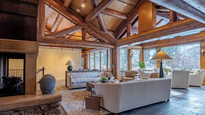 Un vaste salon doté d’une cheminée en pierre, de grandes fenêtres et d’un haut plafond en bois.