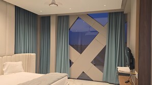 A modern bedroom with a large bed, a TV, and a view of the night sky through a geometric window. - Hotel Annapurna (Ratlam)