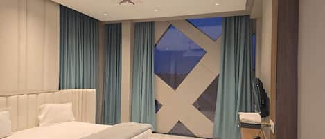 A modern bedroom with a large bed, a TV, and a view of the night sky through a geometric window.