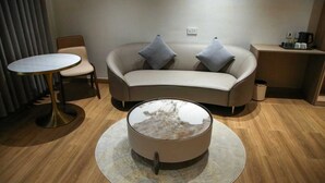 A modern hotel room with a curved sofa, a round coffee table, a small round table, and a side table with a coffee maker. - LEAF HOTEL (Tiruvannamalai)