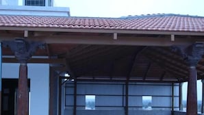 A covered outdoor area with a tiled floor, columns, and a metal fence. - LEAF HOTEL (Tiruvannamalai)