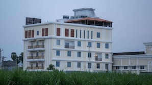 A multi-story building with balconies, a red roof, and a water tower on top. - LEAF HOTEL (Tiruvannamalai)