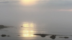Tyyni vesialue, jonka pinnasta heijastuu auringonvalo, ja sen yläpuolella on pilvinen taivas.