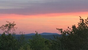 Maisema, jossa näkyy auringonlasku, puita ja kauempana kohoavia kukkuloita.