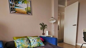 Un dormitorio con cama, sofá azul, un cuadro de playa y una puerta.