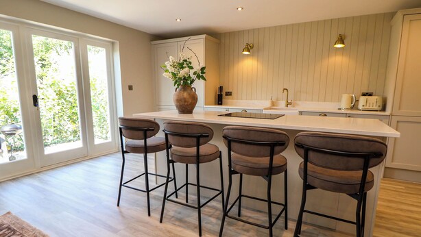 A modern kitchen with a central island, bar stools, and a large window. - Egerton Cottage (Crewe)