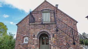 A brick building with a green door, a small window, and a staircase leading to a balcony. - Egerton Cottage (Crewe)