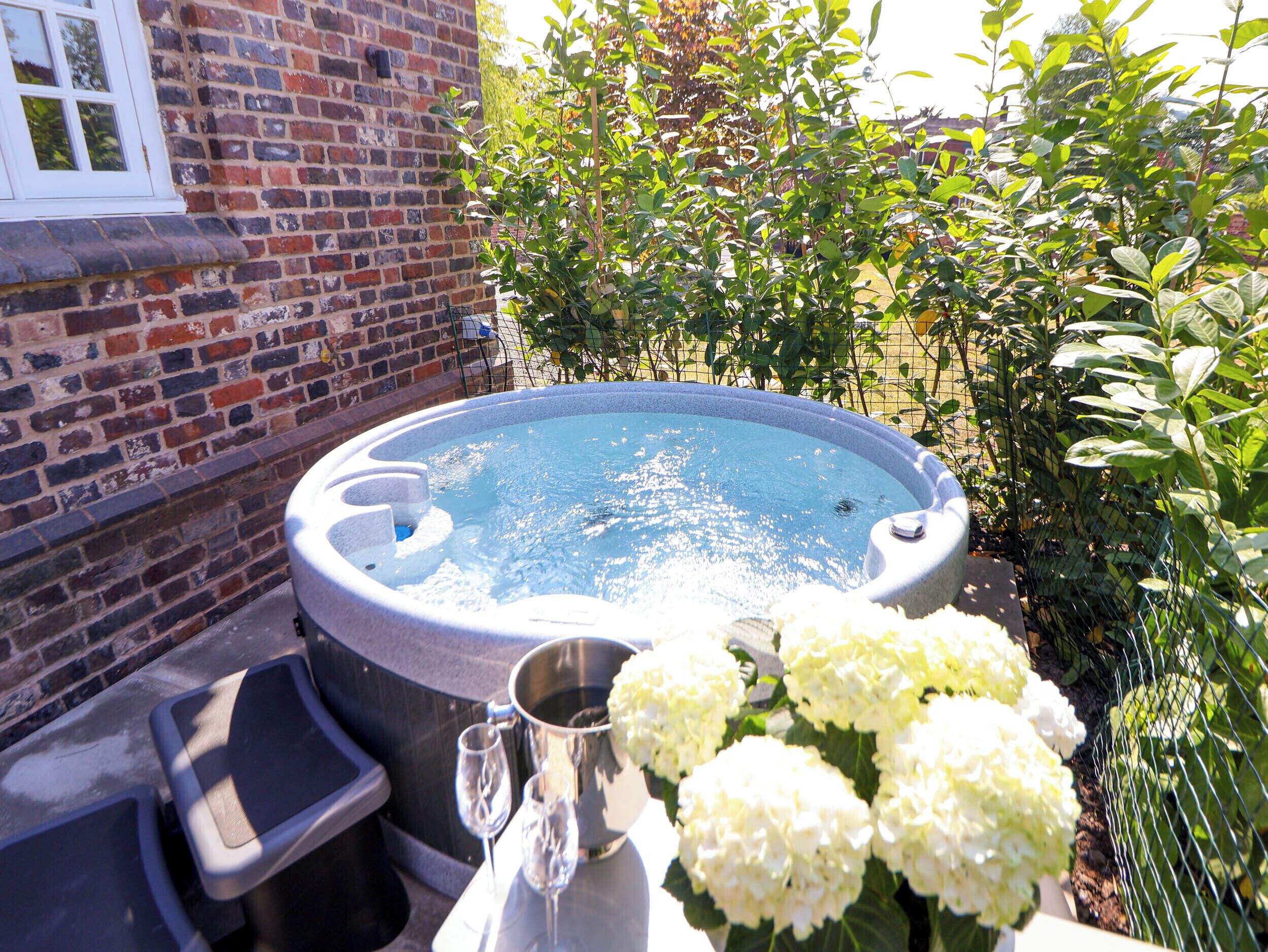 A hot tub with a brick wall and greenery in the background.