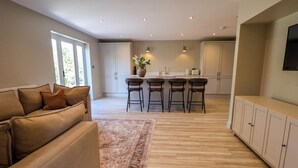 A modern kitchen with a central island, bar stools, and a dining area. - Egerton Cottage (Crewe)
