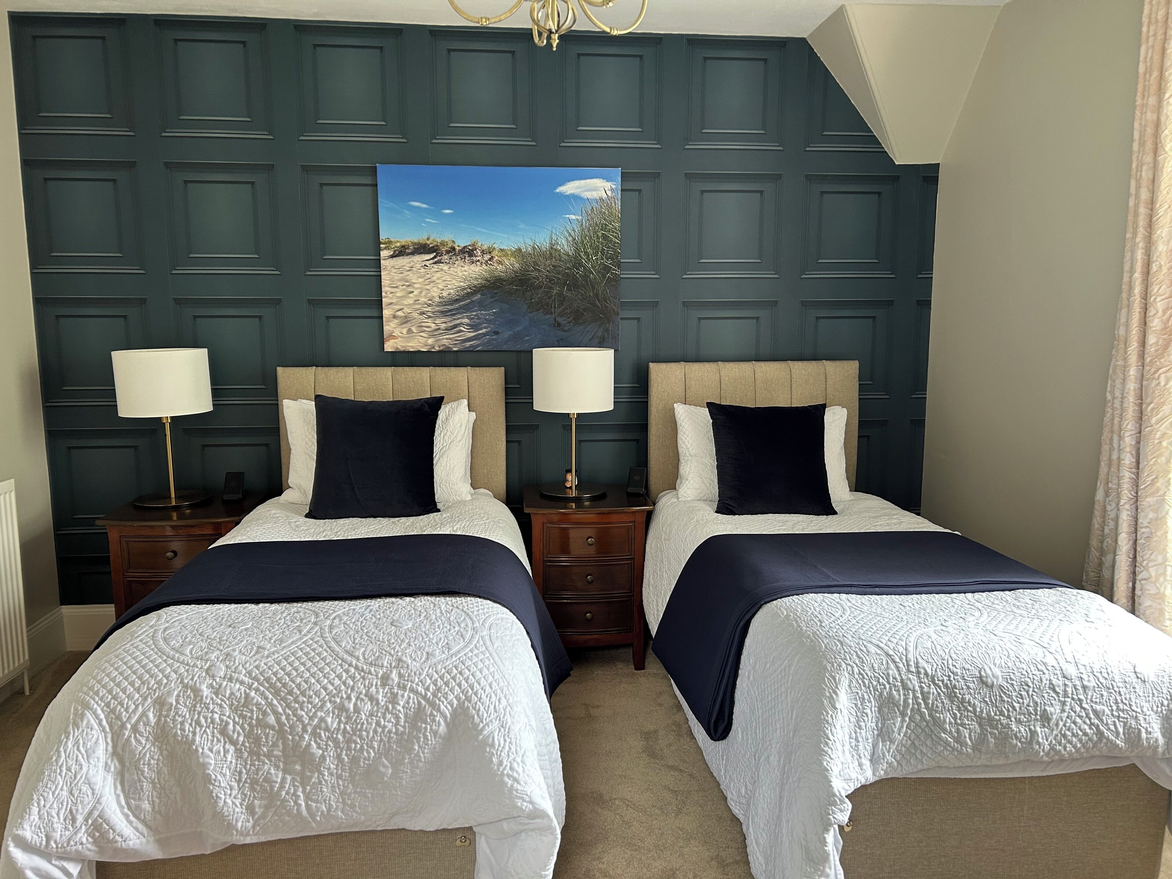 A hotel room with two beds, a painting of a beach, and a chandelier.