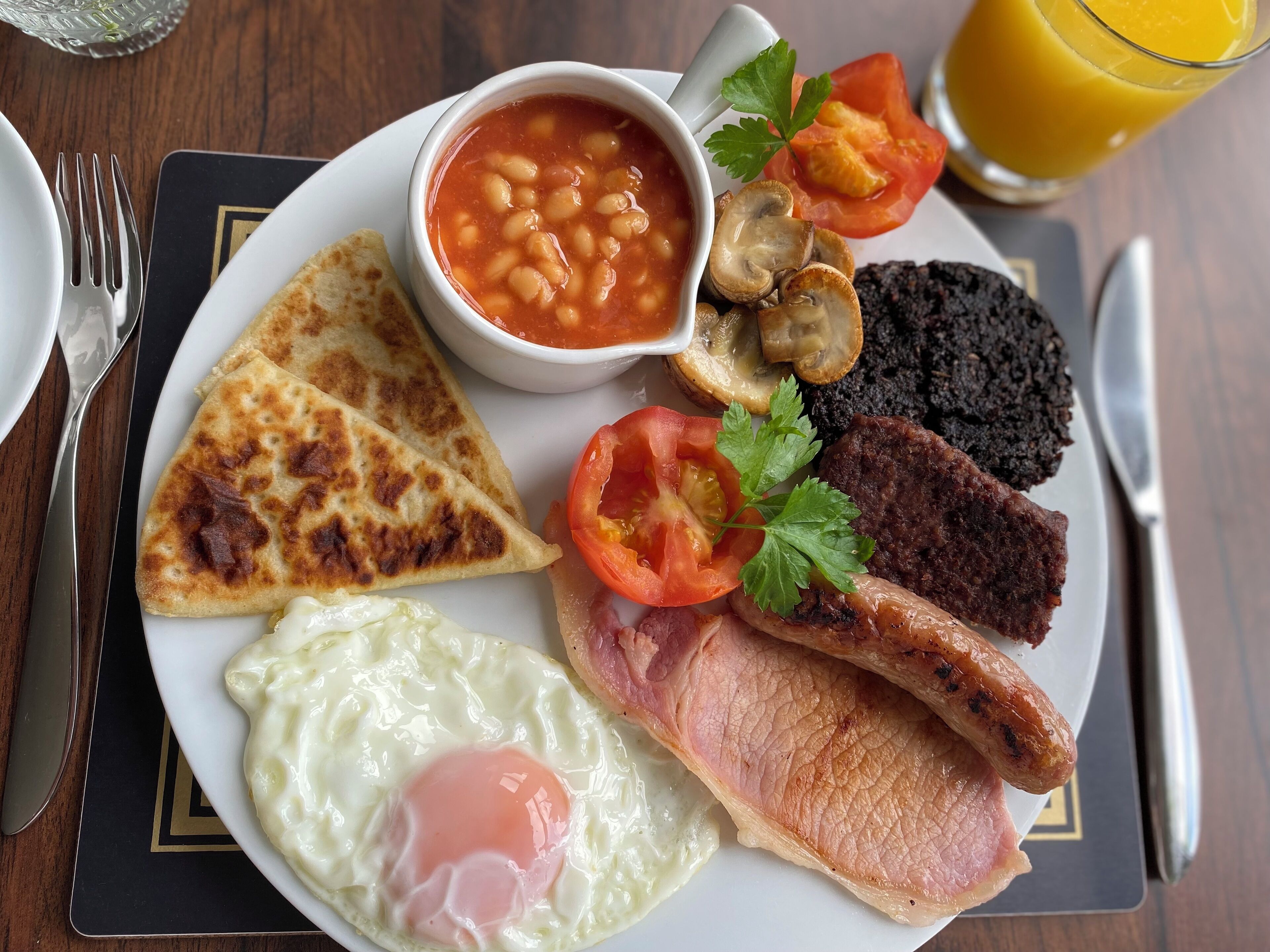 Um prato com ovo frito, bacon, salsichas, cogumelos, tomates e feijão.