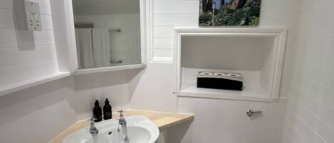 A small bathroom with a white sink, a toilet, a mirror, and a shelf with toiletries.
