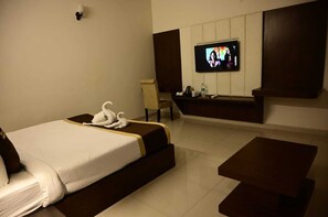 A hotel room with a bed, a TV mounted on the wall, a chair, and a small table. - Hotel Cheer Inn (Lucknow)