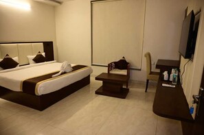 A hotel room with a bed, a chair, a small table, and a TV mounted on the wall. - Hotel Cheer Inn (Lucknow)