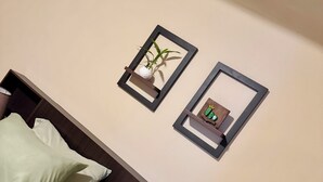 Un letto con cuscini bianchi e una testiera in legno, uno scaffale a parete con una decorazione di cactus e un quadro con un'immagine di una pianta.