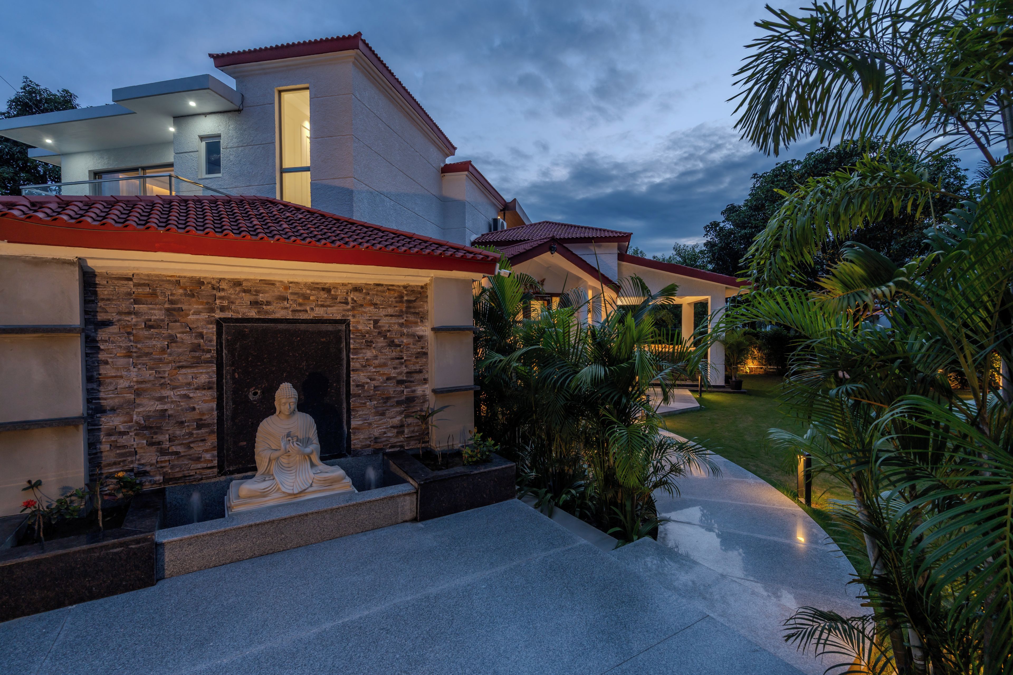 Una casa moderna con fachada de piedra, una estatua y un jardín bien cuidado.