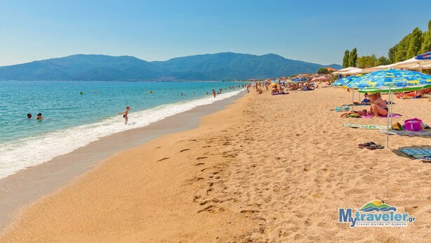 A beach with clear blue water, people swimming and sunbathing, and mountains in the background. - Aigli Garden Retreat, Cozy Escape Close to the Sea (Volvi)