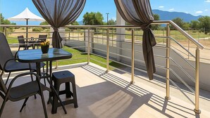 A balcony with a table and chairs, a view of a road, and a mountainous landscape. - Aigli Garden Retreat, Cozy Escape Close to the Sea (Volvi)