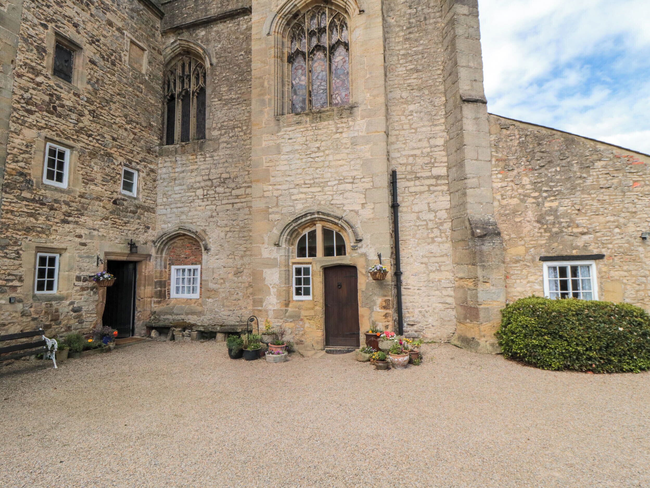A stone building with arched windows and a central door, surrounded by gravel and potted plants.