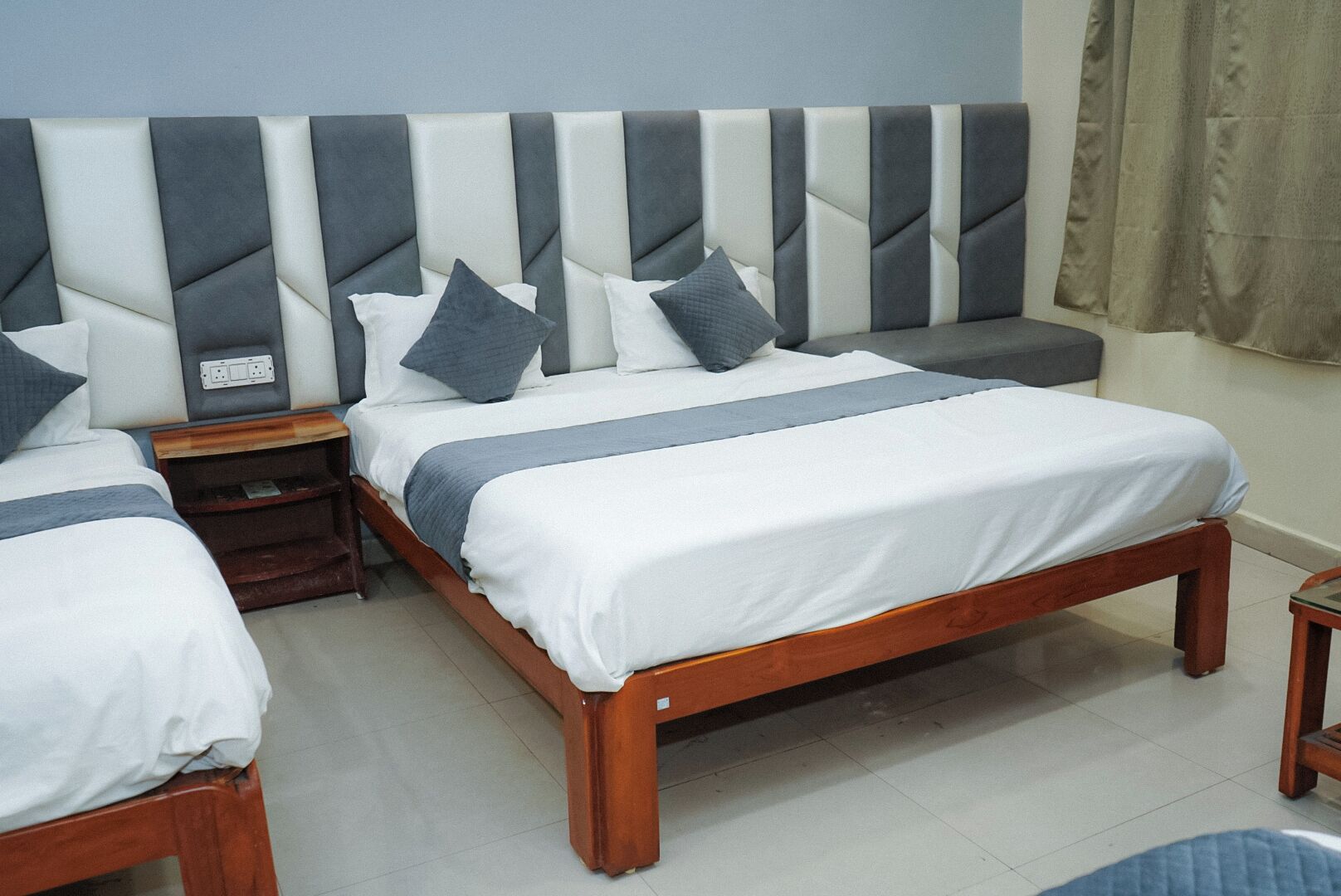 A hotel room with two single beds, a wooden headboard, a bedside table, and a nightstand.