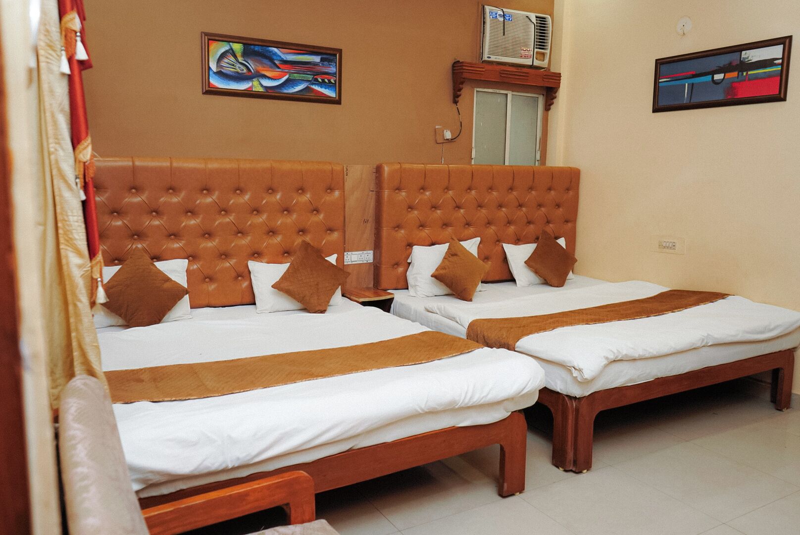 A hotel room with two beds, each with a brown headboard and white bedding. There are two pillows on each bed, and a brown throw blanket is draped over the beds.
