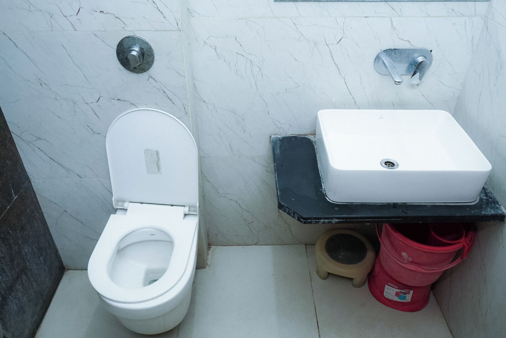 Baño con inodoro, lavamanos y un cubo rojo.