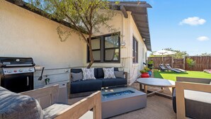 A patio with a barbecue grill, a sofa, a glass-top table, and a wooden bench. - Casa Corazón - Walk to UA (Tucson)