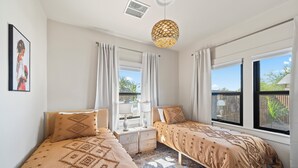 A bedroom with two beds, a window with curtains, a hanging light fixture, and a small table. - Casa Corazón - Walk to UA (Tucson)