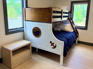 Una cama litera con un ventanal circular, una mesita de madera y vistas a la vegetación.